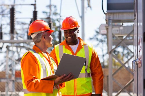 happy electricians using laptop computer in electrical substation